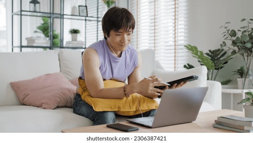 Gen Z Gay queer man non-binary sitting easy relax self study learn online happy work at home sofa. Asia people LGBT young adult guy WFH listen video call reskill upskill in MBA career job school class - Powered by Shutterstock