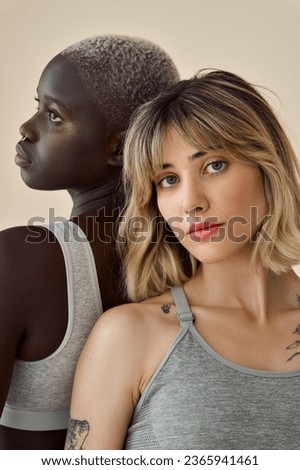 Gen z girls cool diverse inclusive faces beauty models with piercing tattoos short blond hair isolated on beige background. Two African European young women advertising skin care, vertical portrait.