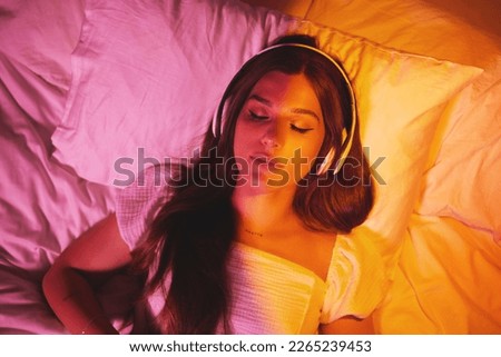 Gen z, headphones and woman sleeping with creative vaporwave lighting in a bedroom bed. Dreaming, music listening and web audio streaming of a female model resting eyes with makeup on a pillow
