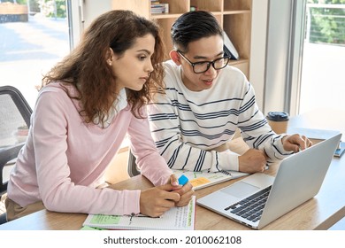 Gen Z Latin Girl And Asian Guy Classmates Talking On Class Work Looking At Laptop Computer. Diverse College Students Discussing Online Project In Classroom. Collaborate International Team Concept.