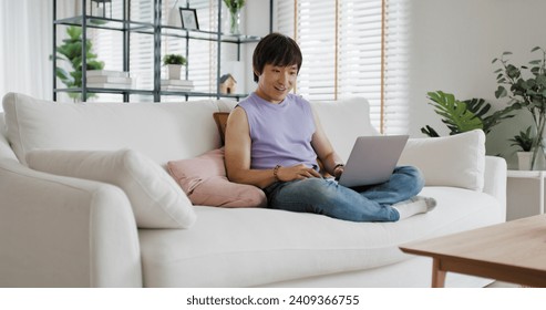 Gen Z queer man non-binary at home. Asia LGBT young guy adult people happy relax sitting at sofa use omni channel easy buy now pay later BNPL shop store. Reading online bank loan news on web page app.