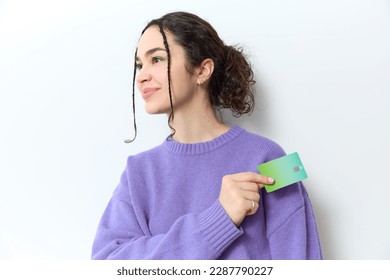 Gen z woman with curly braids and ponytail in purple sweater smiles happily while holding a green credit card to pay in her hand on white backdrop in studio. Shopping online, banking, nfc concept. - Shutterstock ID 2287790227
