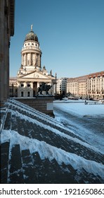 Gendarmenmarkt square in Berlin with French Cathedral, or Franzusischer Dom in German. Picture taken from the steps of Concert Hall on a bright Winter day with blue sky and snow.