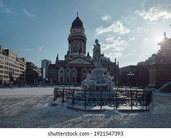 Gendarmenmarkt square in Berlin with German Cathedral, or Deutsche Dom in German. The Schiller Monument, historic statue of Friedrich Schiller in front. Cold winter day with blue sky and snow.
