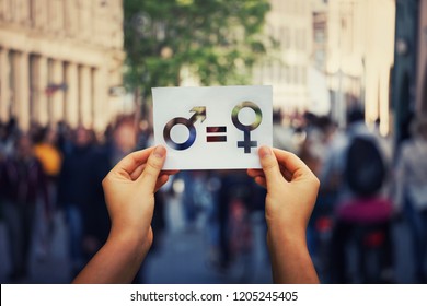 Gender equality concept as woman hands holding a white paper sheet with male and female symbol over a crowded city street background. Sex sign as a metaphor of social issue.