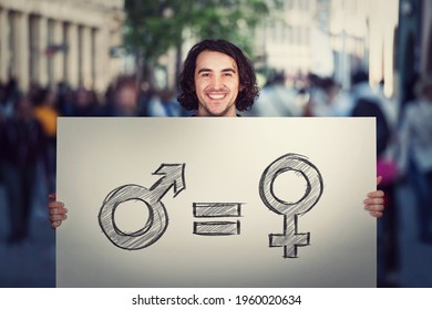 Gender Equality Concept As Young Man Holding A Big Banner With Male And Female Symbol, As Protest Demonstration Message On A Crowded City Street. Sex Rights And Discrimination As A Major Social Issue