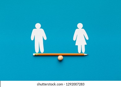 Gender Equality In Corporate World. Figures Of Man And Woman On Pencil Seesaw, Blue Background, Copy Space