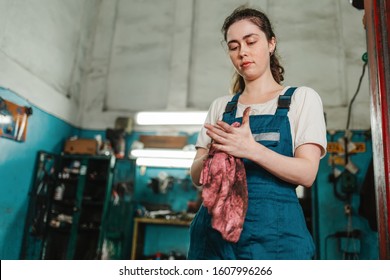 Gender Equality. Portrait Of A Strong Young Woman In Uniform, Working In A Workshop, Which Wipes His Hands With A Rag. Bottom View.Auto Shop In The Background