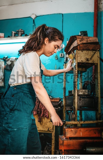 Gender equality. Portrait of a young woman in\
uniform, working near the machine. In the background, a blue wall\
and tools. Vertical