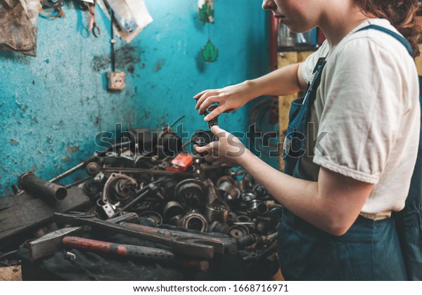 Gender equality. Portrait of a young woman in\
uniform, who is engaged in repairing car parts. Blue wall and spare\
parts in the background. Close\
up