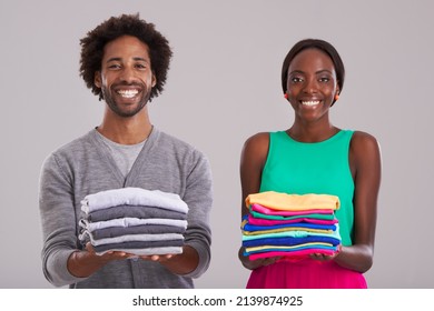 Gender Equality. Studio Shot Of A Young Man And Woman Each Holding A Neatly Folded Pile Of Clothes.