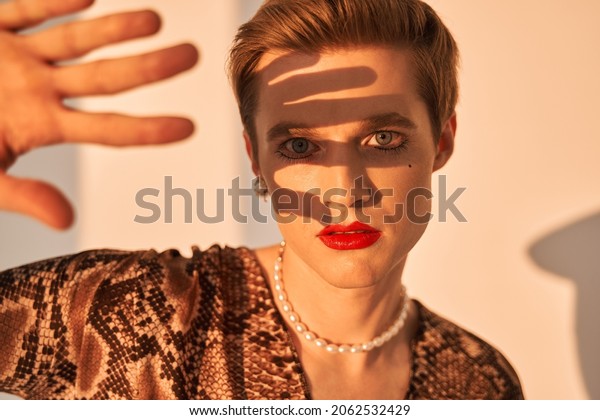 Gender fluid male with makeup and earrings covered\
from the sun with his\
hand
