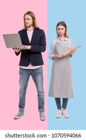 Gender Stereotype. Charming Young Woman In An Apron Posing With A Rolling Pin And Looking Disappointed While Her Boyfriend Working On Laptop