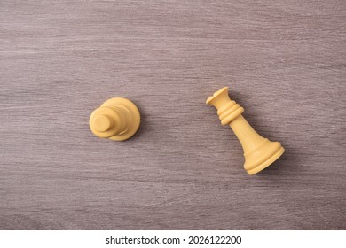 Gender Violence Concept Depicted With Chess King And Queen Piece Lying Down On Wood Table. Top View.