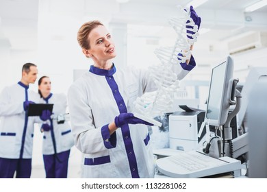 Gene evolution. Positive medical worker keeping smile on her face while looking at molecular chain - Shutterstock ID 1132281062