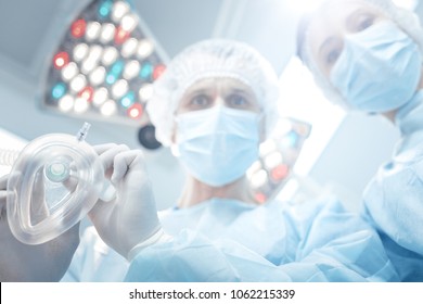 General anaesthesia. Nice professional smart surgeon holding a medical mask and looking at his patient while doing general anaesthesia
