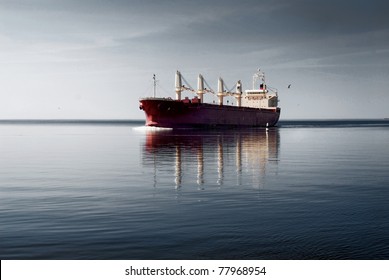 General cargo ship with cranes sailing in a still water. Dramatic sky, dark clouds before the storm. Freight transportation, nautical vessel, global communications, industry, carrying, logistics