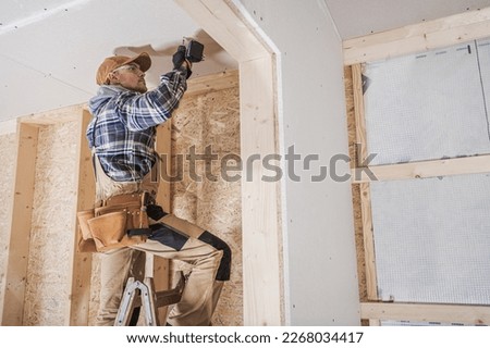 General Construction Contractor Attaching Drywall Using Cordless Drill Driver. Caucasian Remodeling Worker in His 40s.