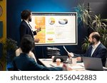 General director showing statistics data on interactive board in a conference, briefing meeting with workers for a presentation. Workmates studying sales reports to adapt within market conditions.