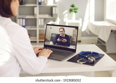 General Practitioner Talking To Senior Patient Via Online Video Conference Chat. Over Shoulder View Laptop Computer Screen On Desk At Doctor's Office. Telemedicine, Virtual Visit To Hospital Concept