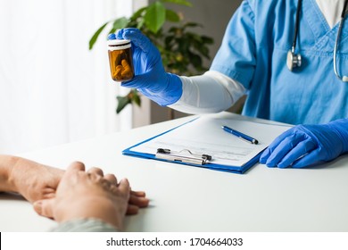 General Practitioner UK GP Doctor Holding Bottle Of Prescription Drugs,handing Over To Patient During Medical Check Up,healthcare Professional Prescribing Treatment Therapy To Elderly Senior Citizen