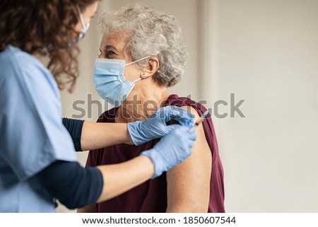 General practitioner vaccinating old patient in clinic with copy space. Doctor giving injection to senior woman at hospital. Nurse holding syringe before make Covid-19 or coronavirus vaccine.