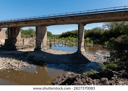 General view of bridge construction site showing pile foundations, stream channel, and existing bridge background