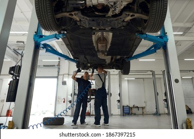 General view of car bottom raised on lift and mechanics working in pair under machine at car service station. Car repairing concept