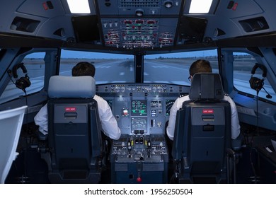General view of the cockpit of a commercial flight simulator, with two pilots sitting in their seats preparing to start the flight during a flight practice - Shutterstock ID 1956250504
