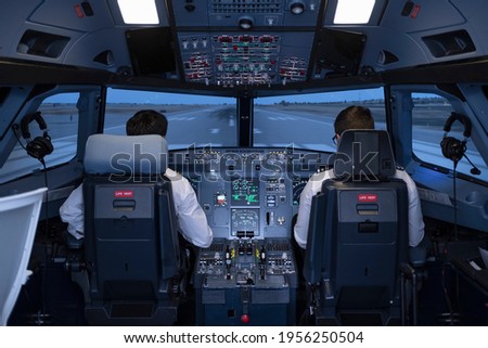 General view of the cockpit of a commercial flight simulator, with two pilots sitting in their seats preparing to start the flight during a flight practice