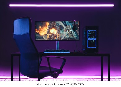 General view of home workplace of pro gamer with professional gaming setup on desktop. Modern powerful PC full RGB light inside, display with shooter game, armchair. Gaming studio of cyber sportsman - Shutterstock ID 2150257027