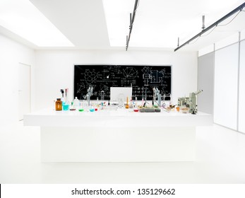 General-view Of A Chemistry Laboratory With A Lab Table Containing Colorful Liquids And Lab Tools And A Blackboard On The Background