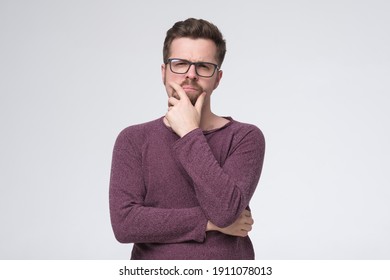 Generating new ideas for you. Thoughtful young man holding hand on chin and looking at camera while standing isolated on white wall - Shutterstock ID 1911078013