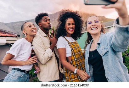 Generation Z Friends Taking A Selfie During A Party On The Rooftop. Group Of Happy Friends Posing For A Group Selfie While Holding Beer Bottles. Multicultural Friends Having Fun Together On The Weeken