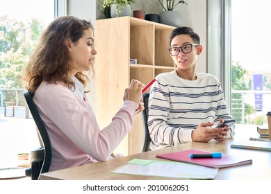 Generation Z Teenagers Male Asian And Latin Girl Using Mobile Cell Smartphone Talking In Classroom. Two Multiethnic Diverse College Students Holding Phone Discussing Social Media And Education Apps.