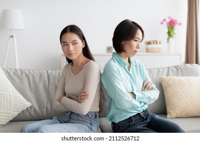 Generations conflict, family problems concept. Offended young Asian woman and her mature mother sitting back to back on couch after argument, not speaking, ignoring each other at home