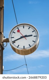 Generic analog clock outside train station platform in Europe. Close, looking up shot, blue sky background, no people