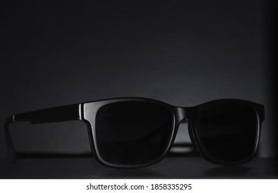 Generic black sunglasses in front of black backdrop