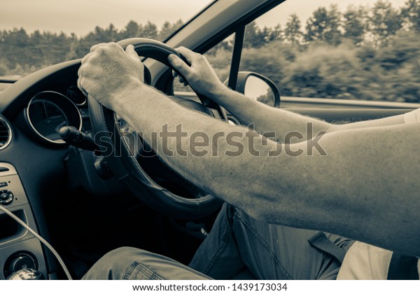 A generic photo of a\
man\'s hands holding a steering wheels in motion with vintage tone.\
Black dashboard with phone charger lead showing. Trees and sky\
through the windows.