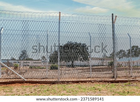 generic view of a prison fence with razor wire and barber wire rolls in top exterior yard