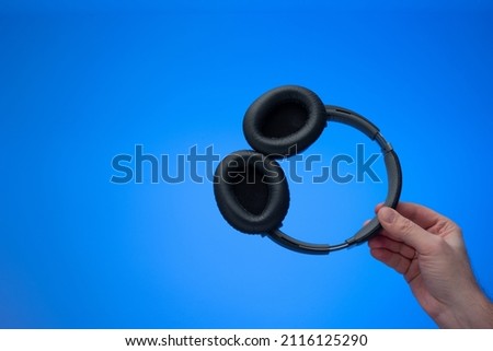 Generic wireless over the ear headphone held in hand by Caucasian male hand. Close up studio shot, isolated on blue background.