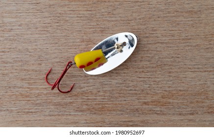 Generic yellow and red spots spinning fishing lure with a treble hook on a wood background.
