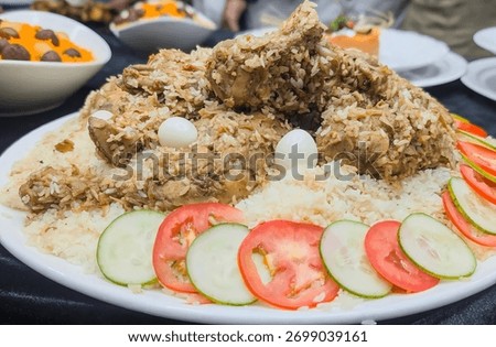 A generous, elevated serving of rich Chicken Biryani (or Pilaf) featuring tender chicken pieces and long-grain, aromatic Basmati rice, generously mounded on a large white platter.