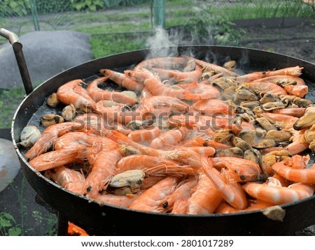A generous portion of succulent shrimp and briny mussels are sizzling in a large black pan, releasing aromatic steam as they cook over a vibrant flame