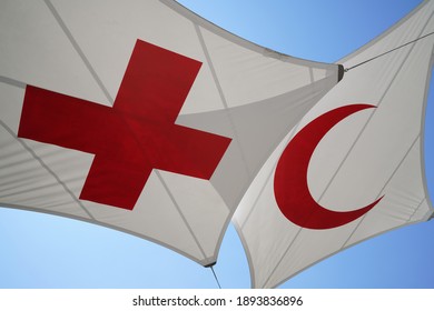 Geneva, Switzerland - July 16 2019:                  A red cross flag hanging with a red crescent flag with clear blue sky on the background