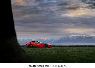 Geneva, Switzerland - March 2020: Red Ferrari F12 TdF Italian rosso supercar parked on fied by Lake Geneva (Lac Léman) during sunset  with Swiss alps in the background