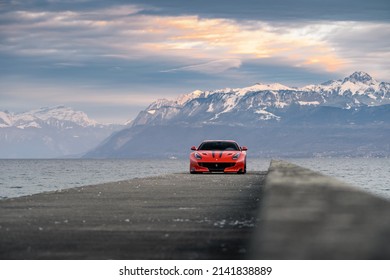 Geneva, Switzerland - March 2020: Red Ferrari F12 TdF Italian rosso supercar parked on pier by Lake Geneva (Lac Léman) during sunset  with Swiss alps in the background
