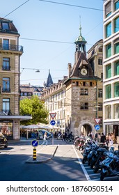 Geneva, Switzerland - September 8, 2020: The Molard Tower Or Clock Tower, Which Was Part Of The Fortified Wall Of The City, Is Overlooking The Busy Molard Square With Sidewalk Cafes And Restaurants.