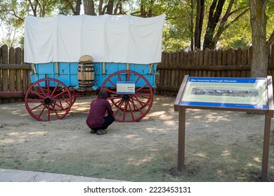 Genoa, NV, USA. 2022-09-17. Unidentified Young Man Looking At A Blue Prairie Schooner Wagon With Red Wheels At The Mormon Station Historic Park. 