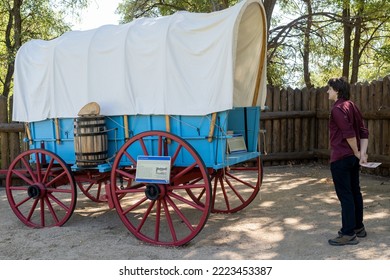 Genoa, NV, USA. 2022-09-17. Unidentified Young Man Looking At A Blue Prairie Schooner Wagon With Red Wheels At The Mormon Station Historic Park. 